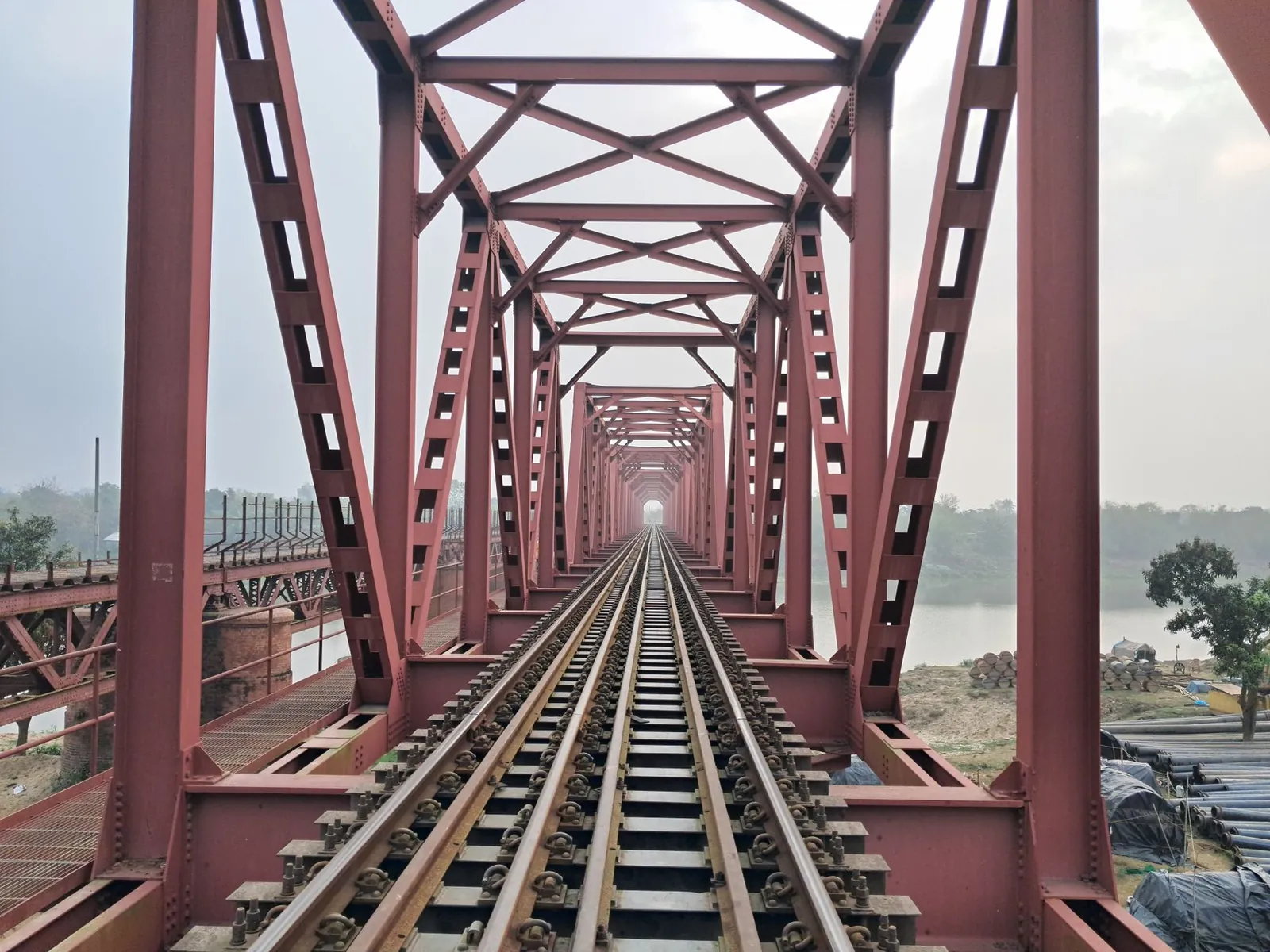 A striking perspective view of a red railway bridge spanning across a calm river. Stock photo illustrating GPT Infraprojects' new order story.