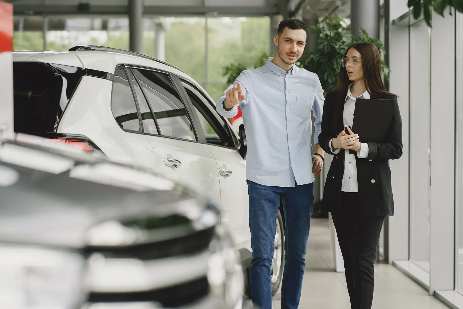 Customer and salesperson discussing a vehicle inside a modern car dealership showroom. Stock photo illustrating CarTrade Tech's product launched story.
