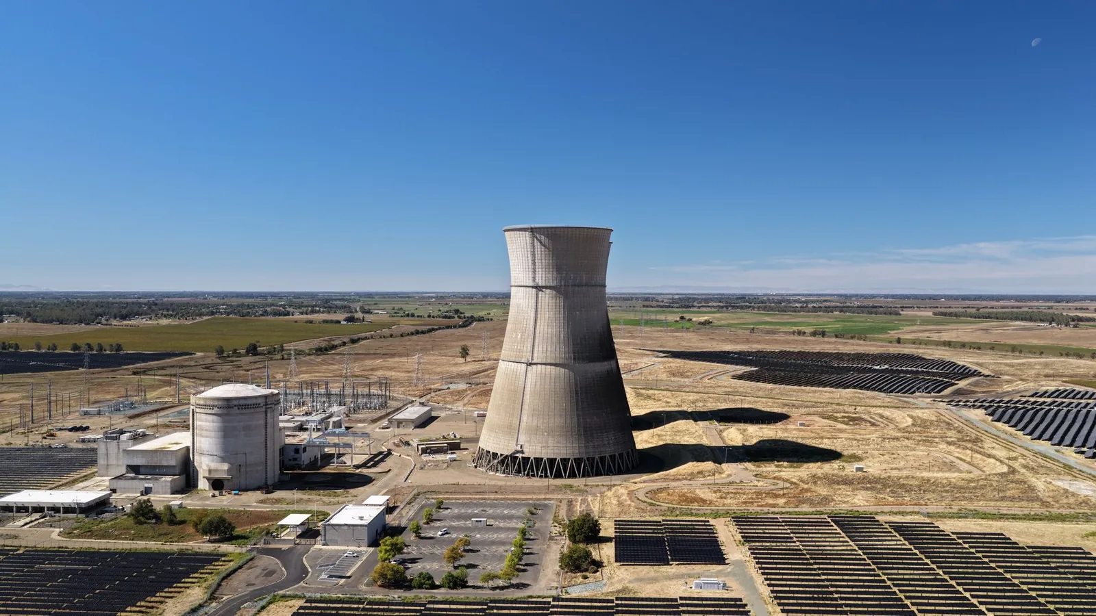Aerial view of a cooling tower surrounded by solar panels in a rural landscape. Stock photo illustrating Bondada Engineering's regulatory approval story.