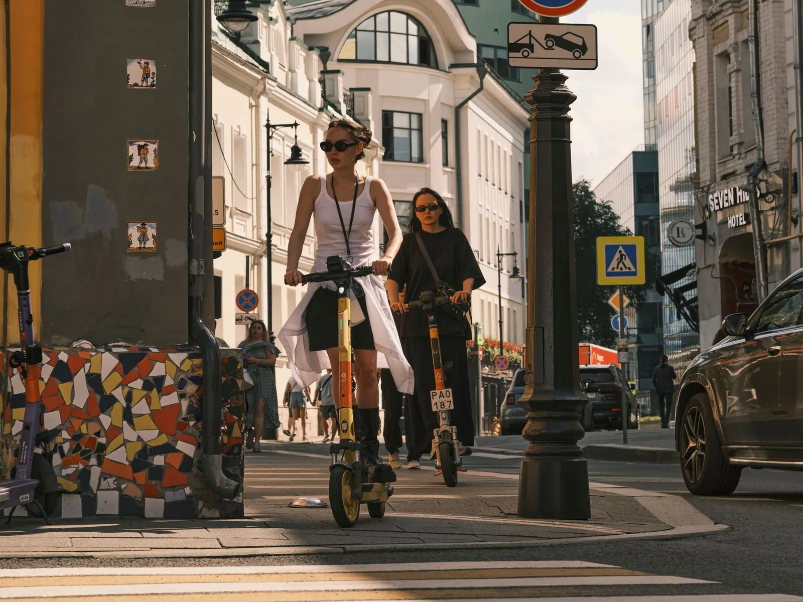 Two women riding electric scooters on a city street, showcasing urban commute. Stock photo illustrating Zelio E-Mobility's fund raise story.