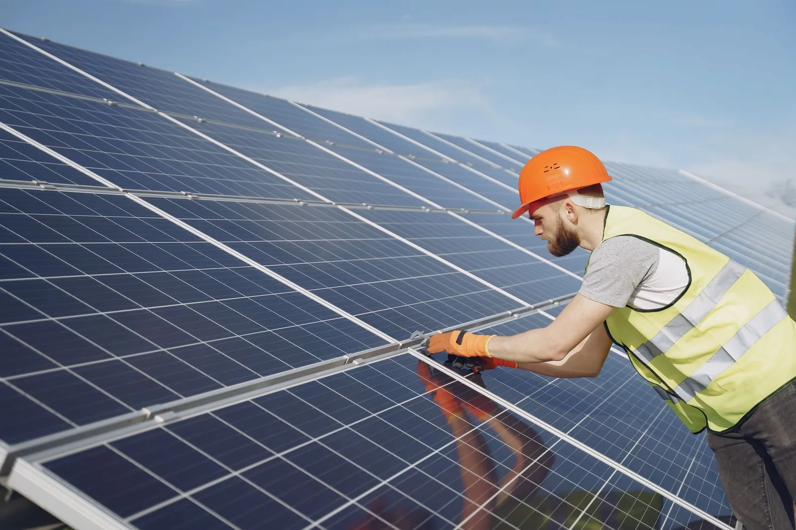 Side view of focused young man in uniform and hardhat checking setup of solar panels. Stock photo illustrating Emrock Corporation's new order story.