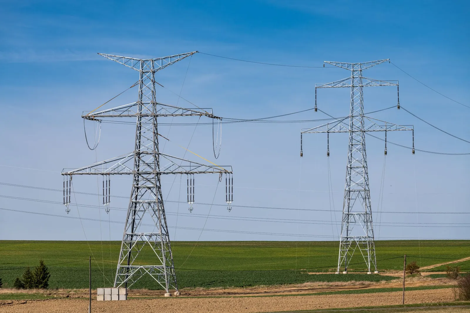 Scenic rural landscape featuring high voltage transmission towers under a clear blue sky. Stock photo illustrating Om Power Transmission's earning call story.