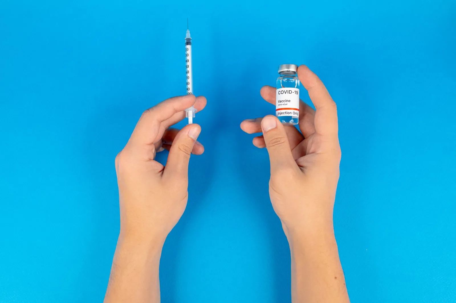 Close-up of hands holding a COVID-19 vaccine vial and syringe against a blue background. Stock photo illustrating Lupin's product launched story.