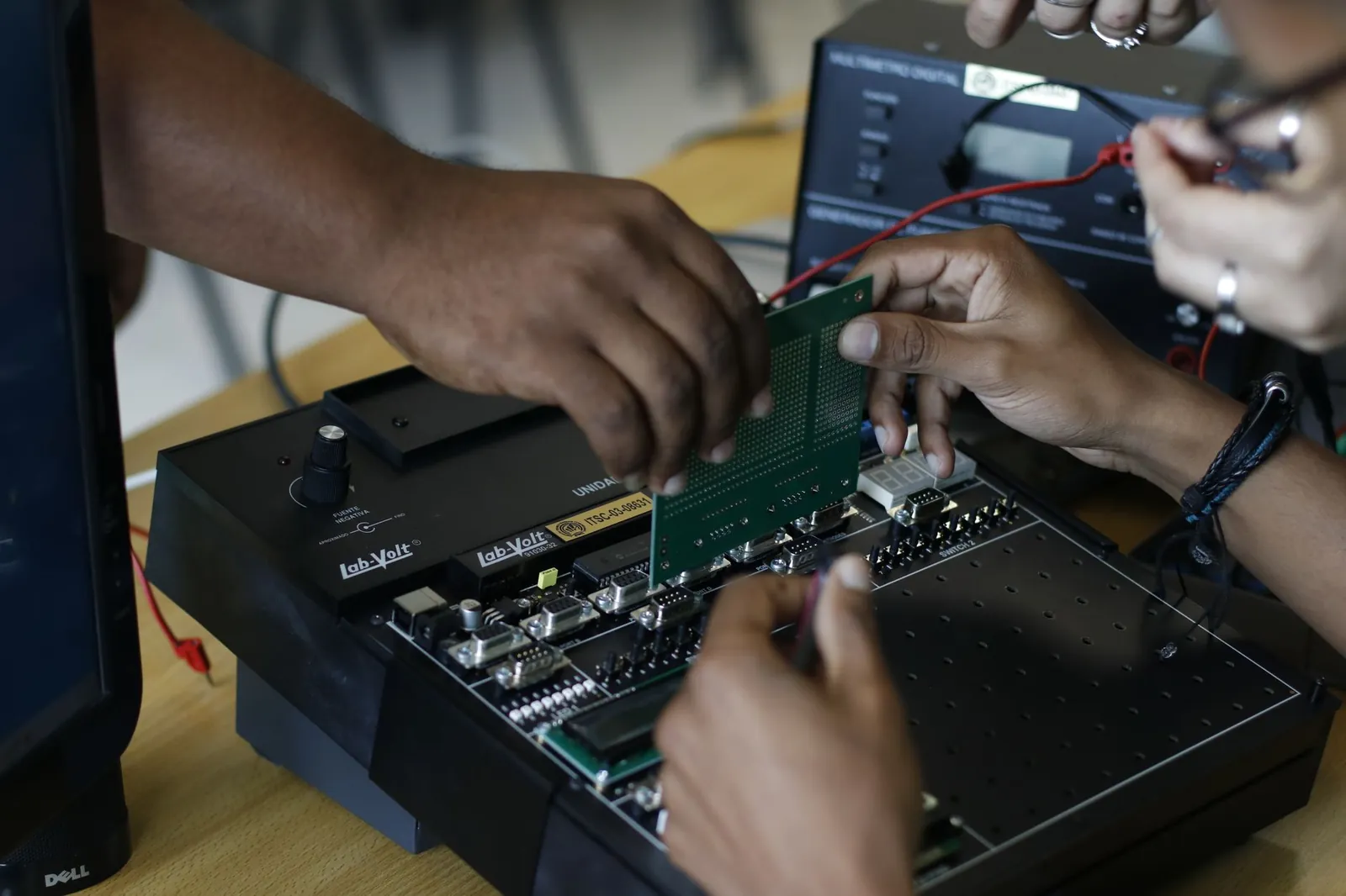 Close-up of hands assembling an electronic circuit board, showcasing teamwork and technical expertise. Stock photo illustrating Aimtron Electronics' fund raise story.