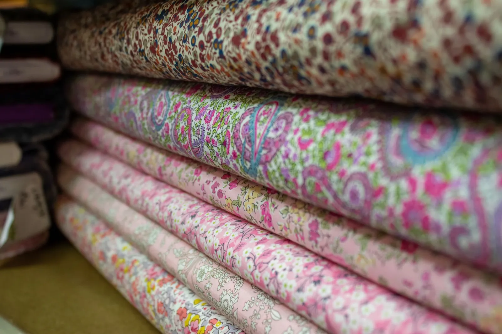 Vibrant floral and patterned fabric rolls stacked in a textile store. Stock photo illustrating Tuni Textile Mills' new order story.