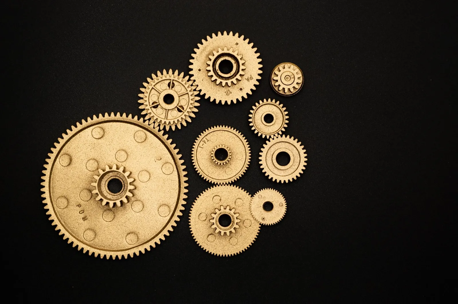 Close-up of golden gears and cogs arranged on a black background, representing teamwork and industry. Stock photo illustrating Shanti Gold International's production started story.