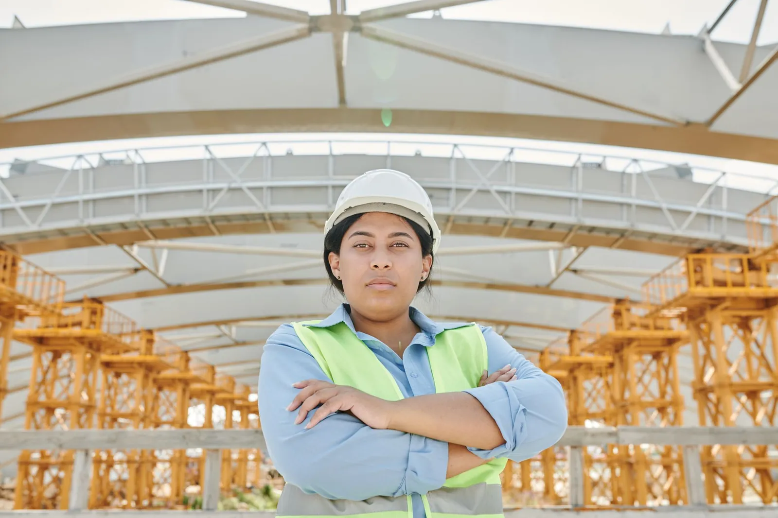 Female engineer in safety gear at a construction site with steel structure background. Stock photo illustrating JSW Steel's expansion story.
