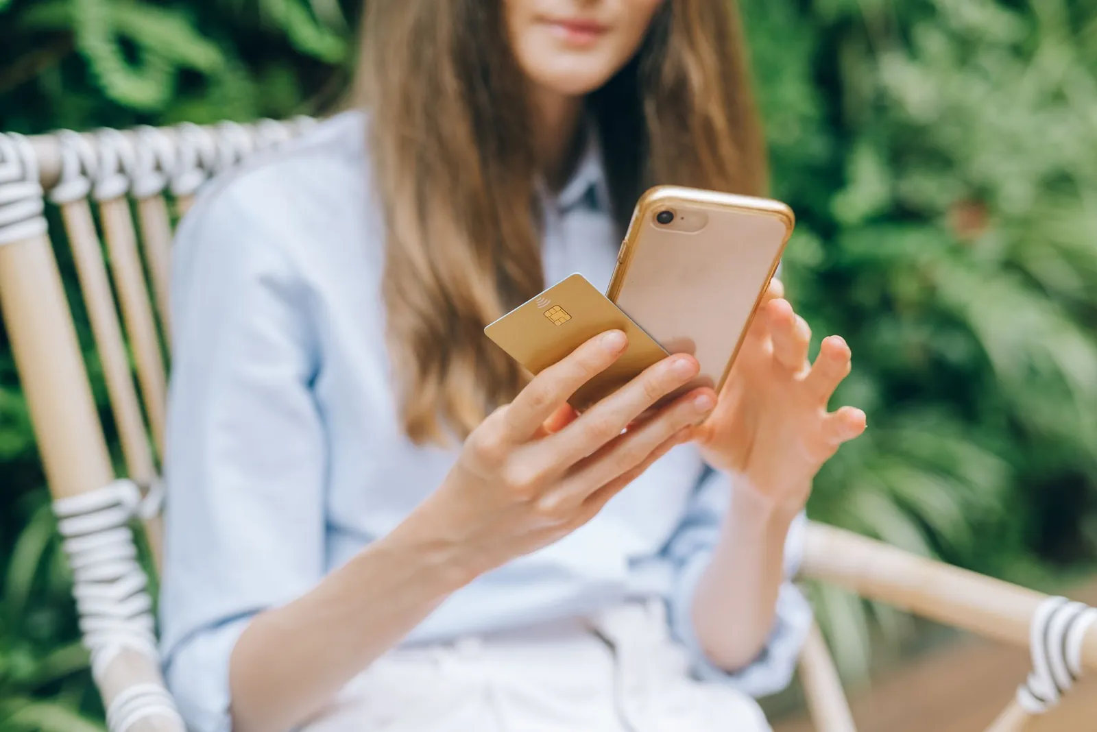 A woman making an online purchase using a smartphone and credit card outdoors. Stock photo illustrating Intellect Design Arena's product launched story.