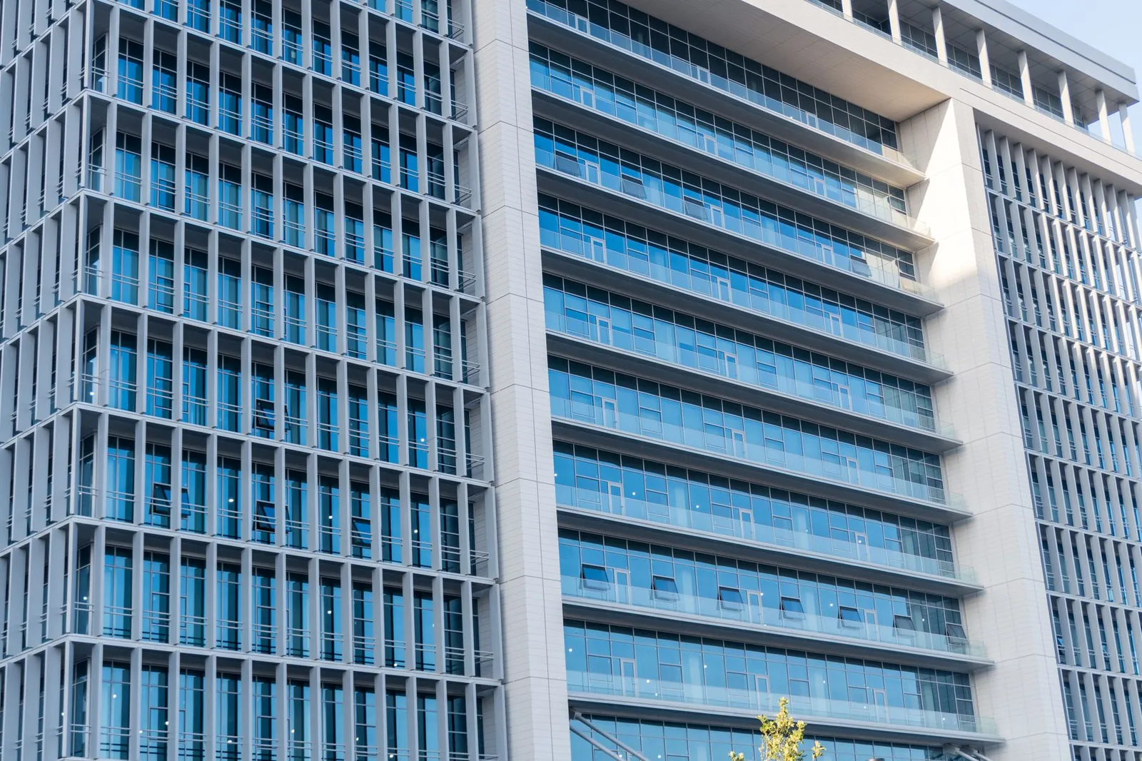 A modern office building with glass facade, featuring urban city architecture and blue sky reflections. Stock photo illustrating Suraj Estate Developers' expansion story.