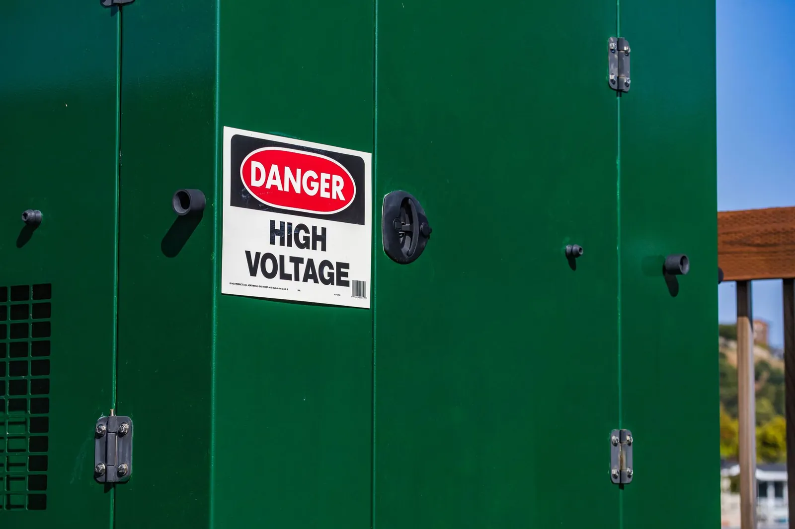 Green electrical box with warning 'Danger High Voltage' sign under clear sky. Stock photo illustrating CG Power and Industrial Solutions' production started story.