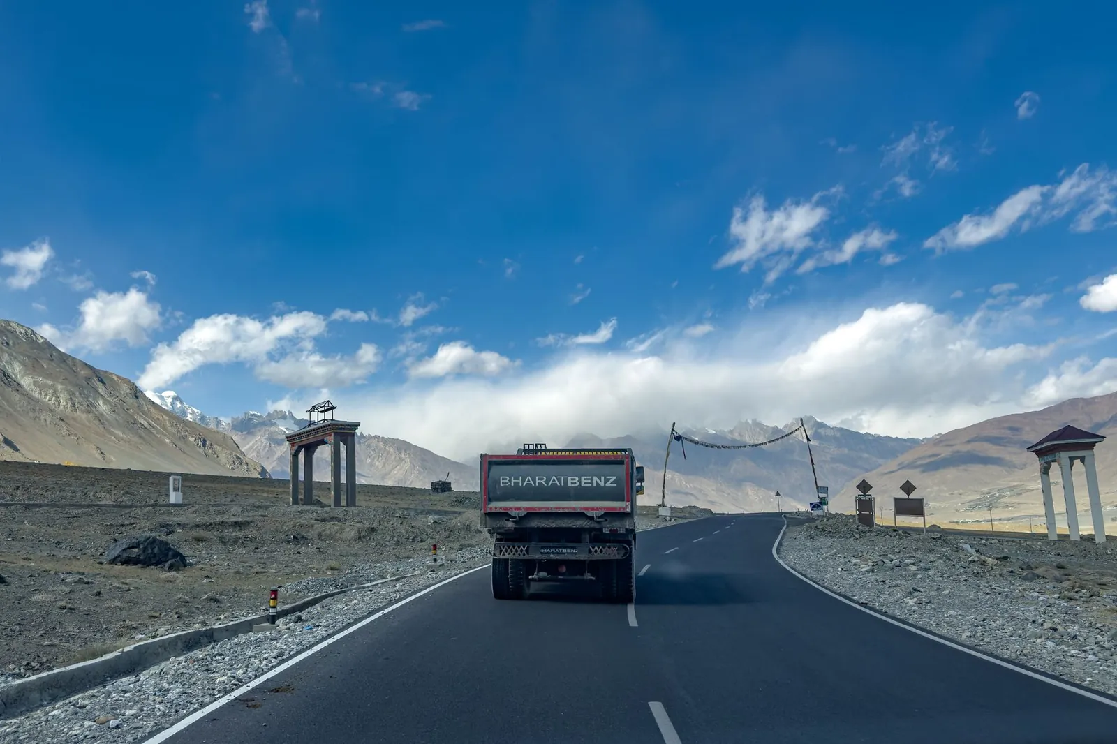 A BharatBenz truck travels on a scenic mountainous road under a clear blue sky. Stock photo illustrating Ceigall India's new order story.