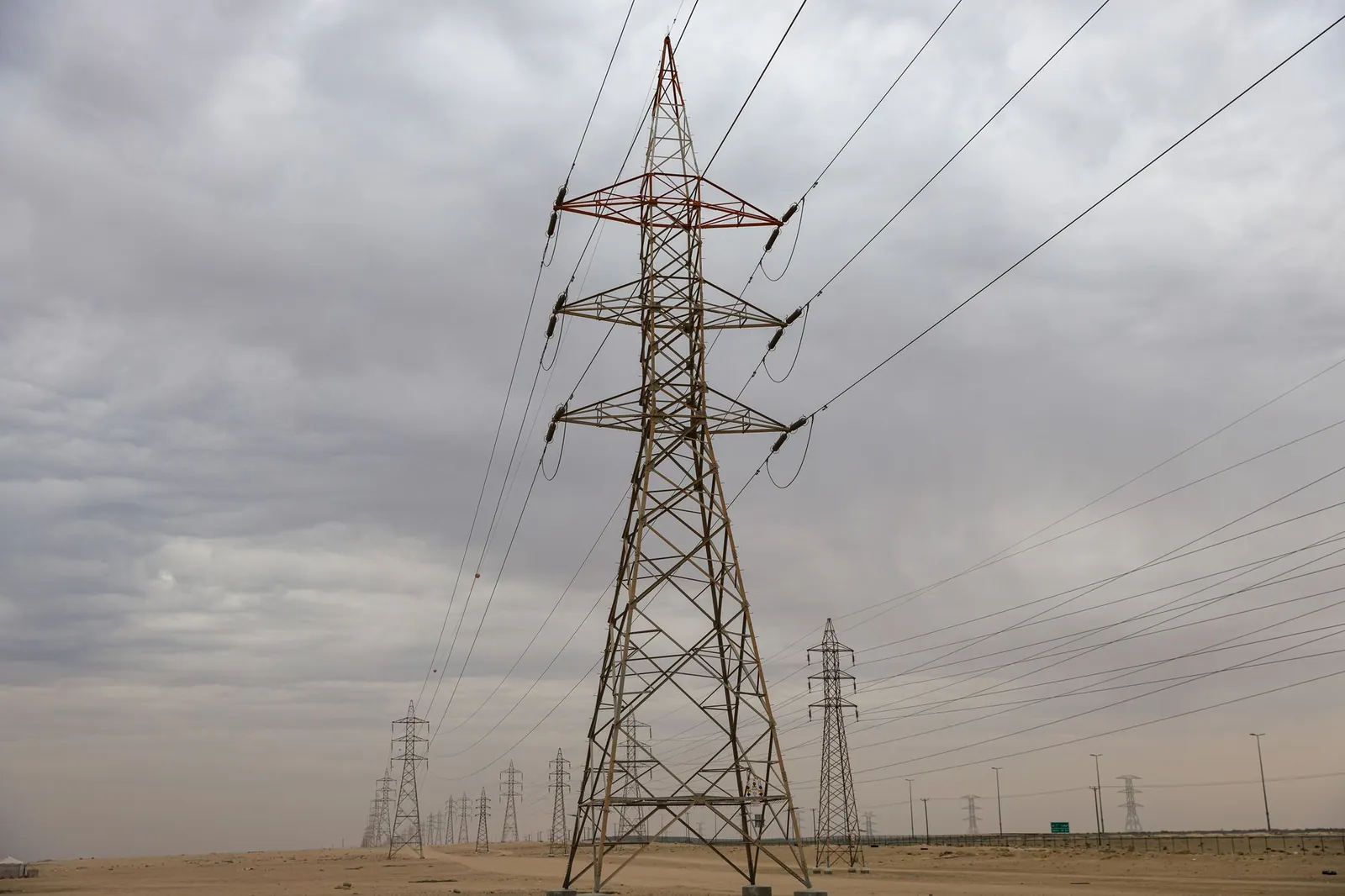 Power transmission towers under a cloudy sky spanning across a desert landscape, showcasing industrial infrastructure. Stock photo illustrating Jyoti Structures' new order story.