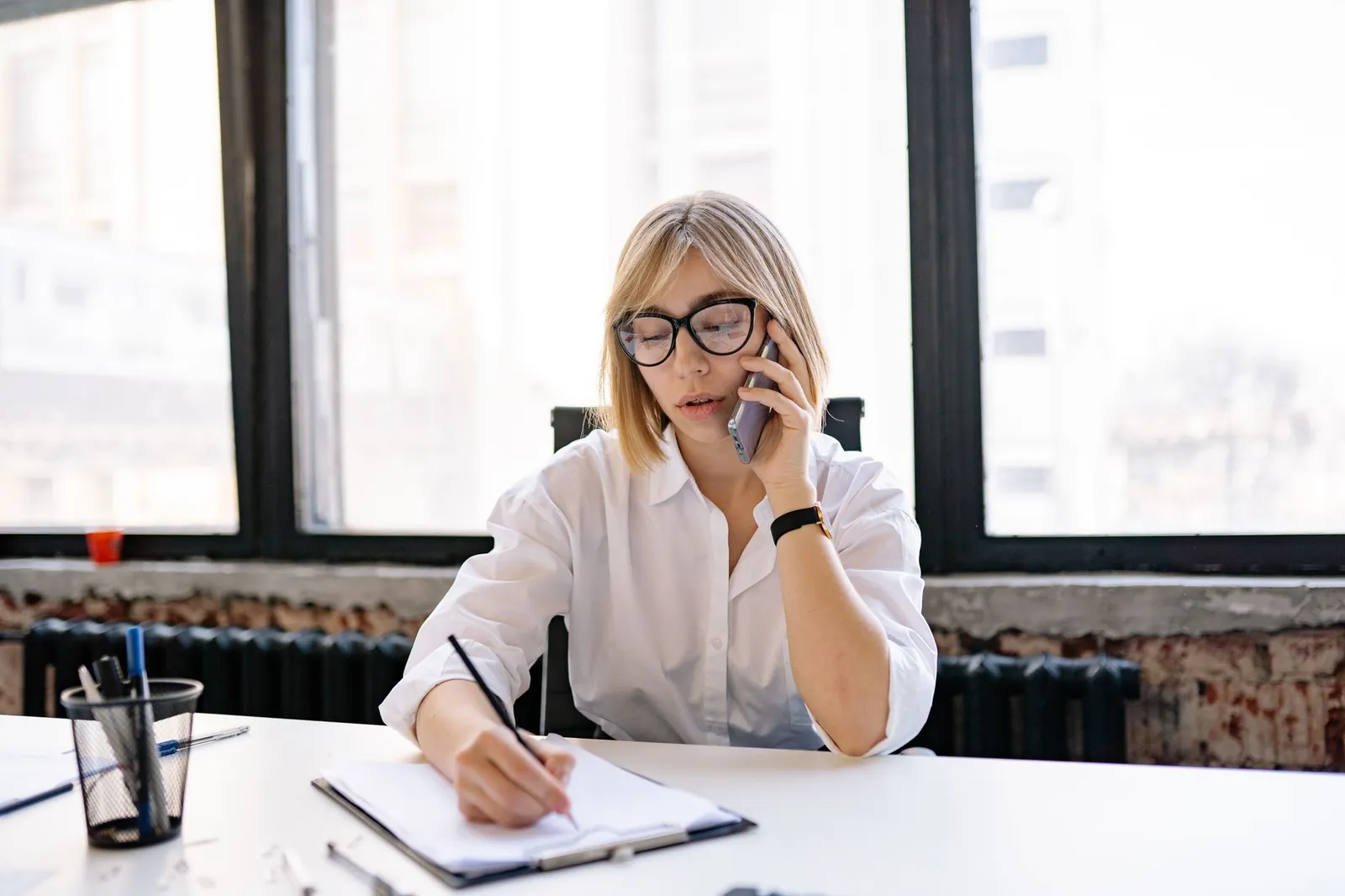 A woman in an office setting multitasking with a phone call and taking notes. Stock photo for the ALFA News guide: How to Find and Read an Earnings Call Transcript in India.