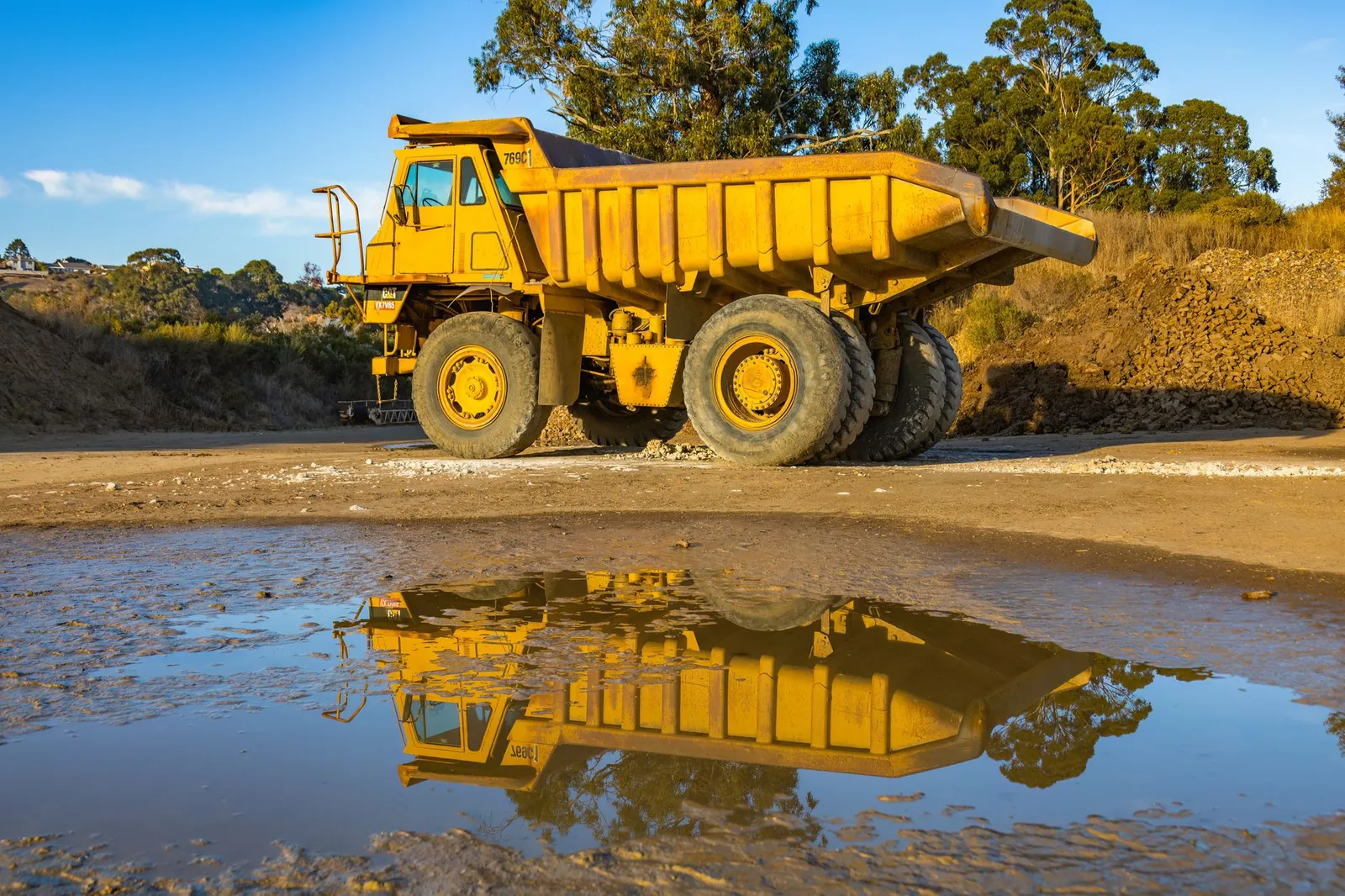 Yellow dump truck with reflection in water at a mining site, exhibiting industry machinery. Stock photo illustrating BEML's product launched story.