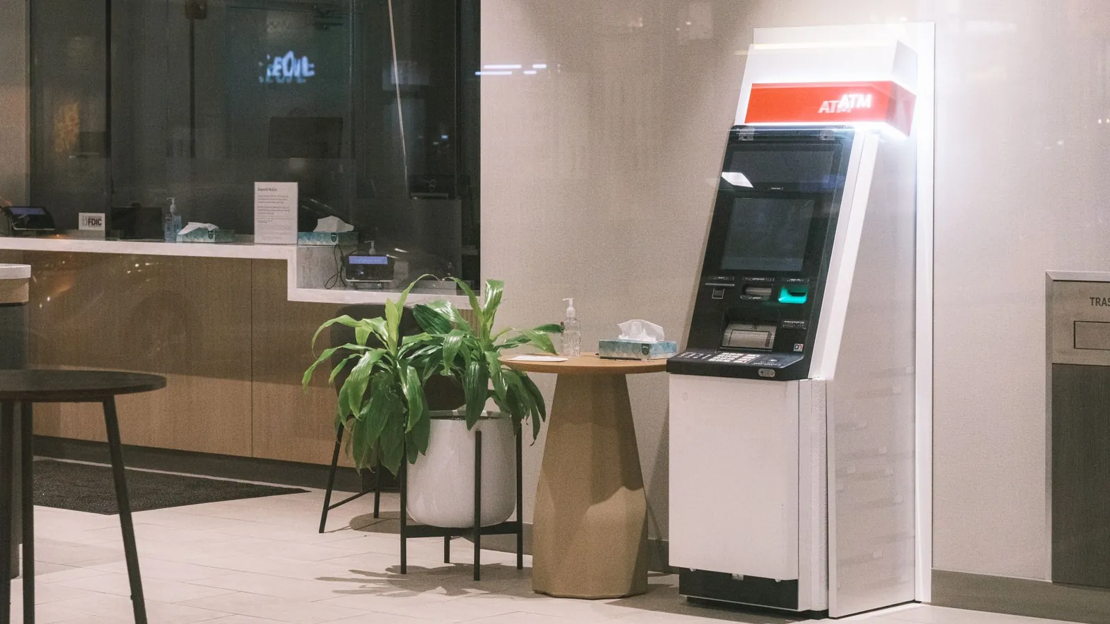 An ATM machine stands in a modern bank lobby, next to a plant and table. Stock photo illustrating Jana Small Finance Bank's earning call story.