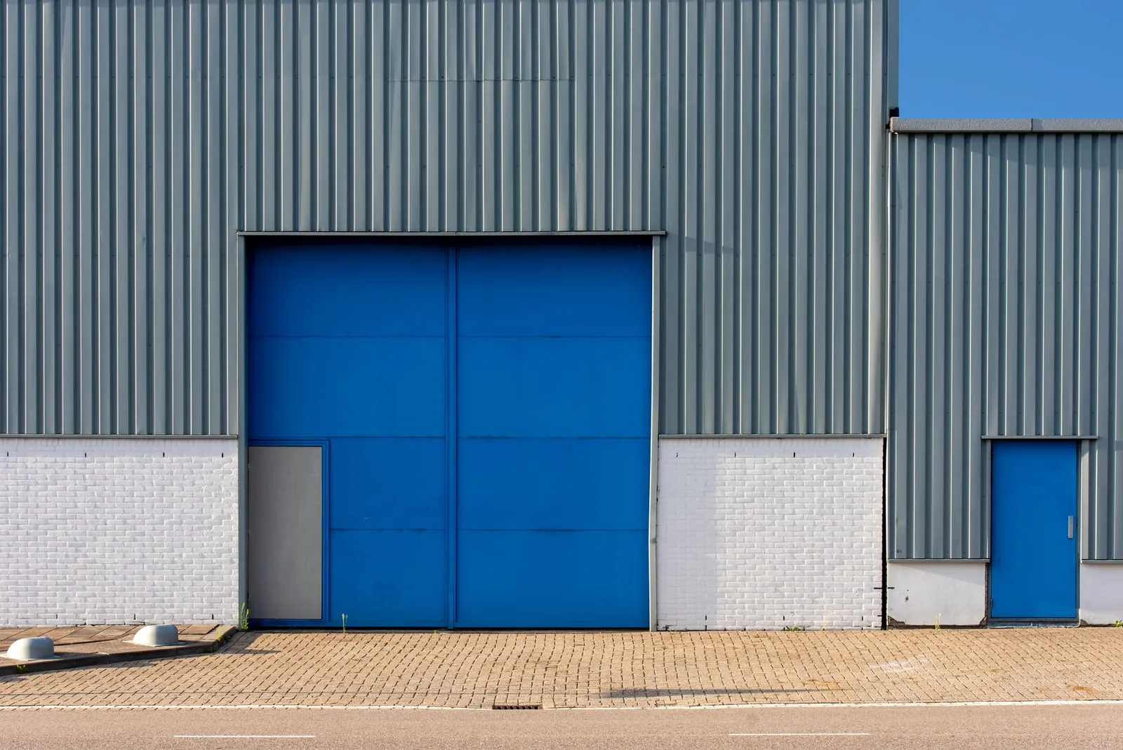 Front view of a blue and gray metal warehouse exterior with large doors. Stock photo illustrating Om Freight Forwarders' expansion story.