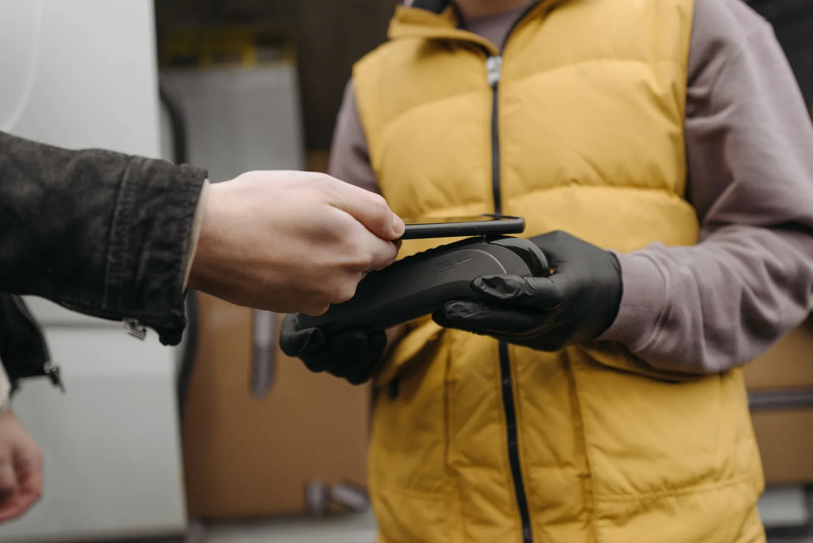 A close-up of a contactless payment made using a cellphone and a payment terminal held by a courier. Stock photo illustrating Aurionpro Solutions' partnership story.