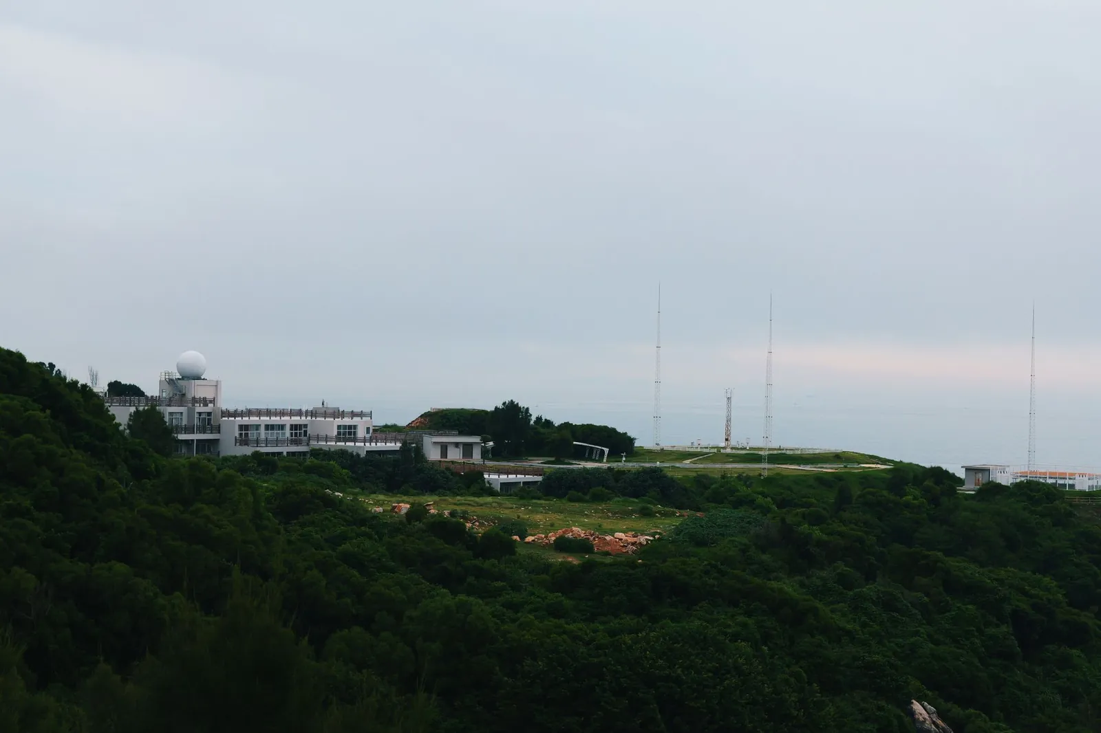 A distant radar station sits atop a lush green hill under an overcast sky. Stock photo illustrating Marine Electricals (India)'s partnership story.