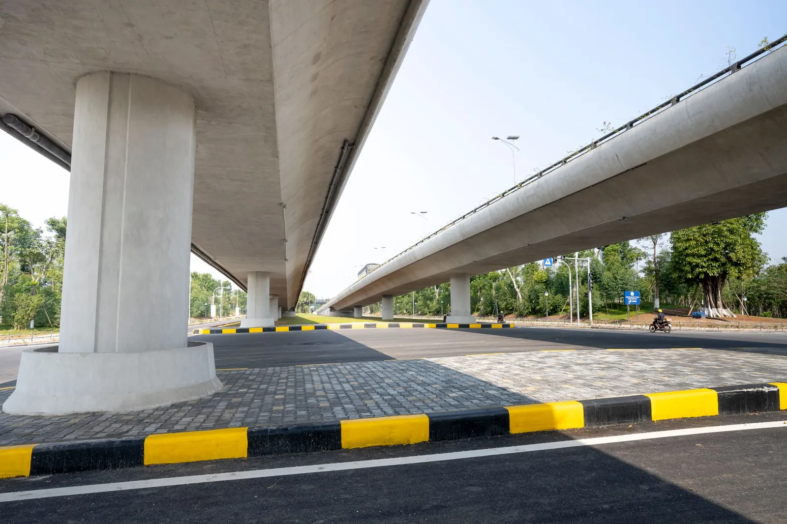 Concrete elevated roadways over asphalt highway between verdant greenery in suburban area on sunny day. Stock photo illustrating PNC Infratech's new order story.