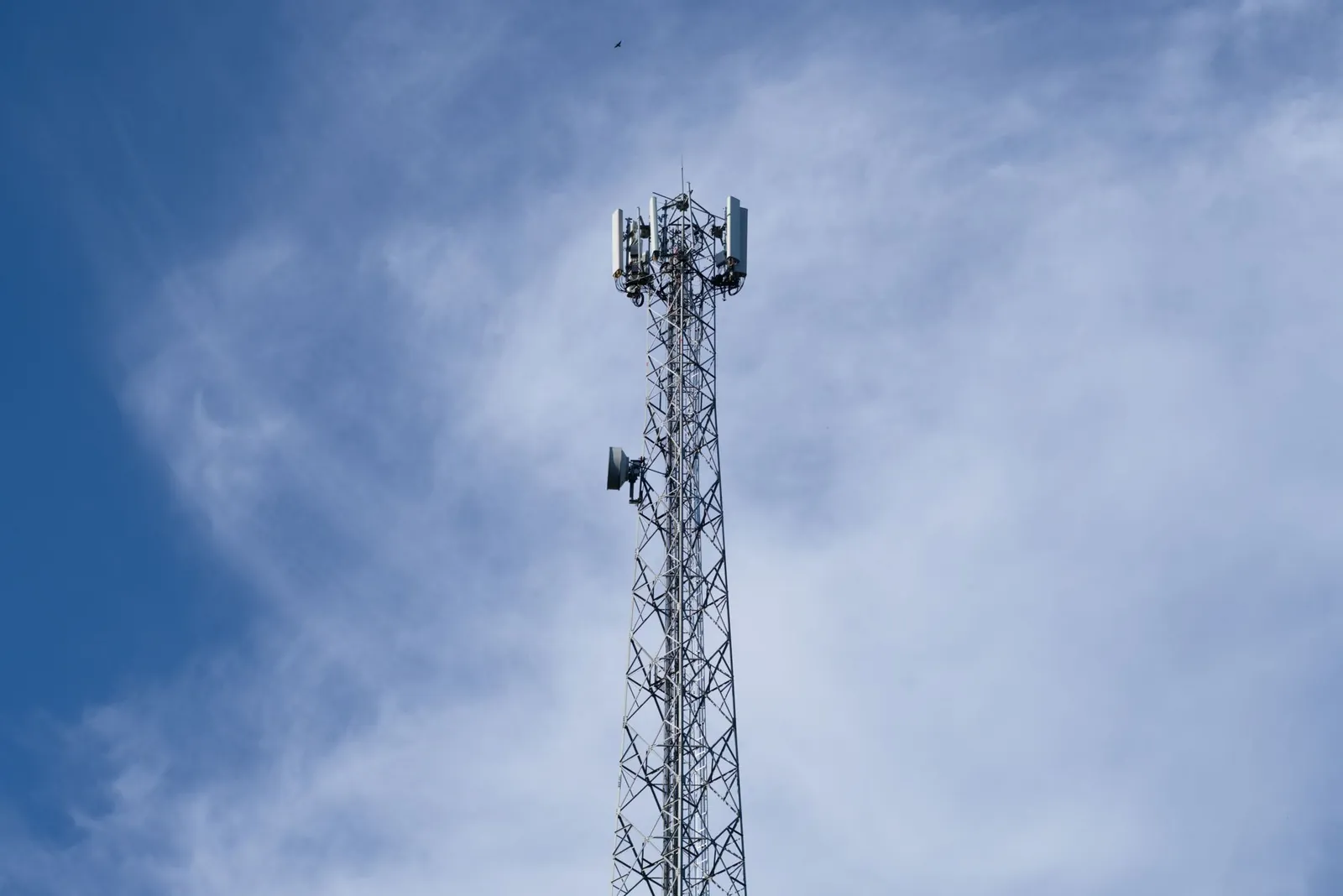 A tall metal communications tower stands against a backdrop of a clear blue sky with scattered clouds. Stock photo illustrating ITI's new order story.