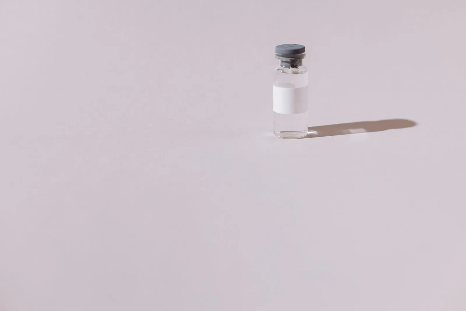 A sterile vaccine vial isolated on a minimalist gray background, emphasizing health and medicine. Stock photo illustrating Shilpa Medicare's regulatory approval story.