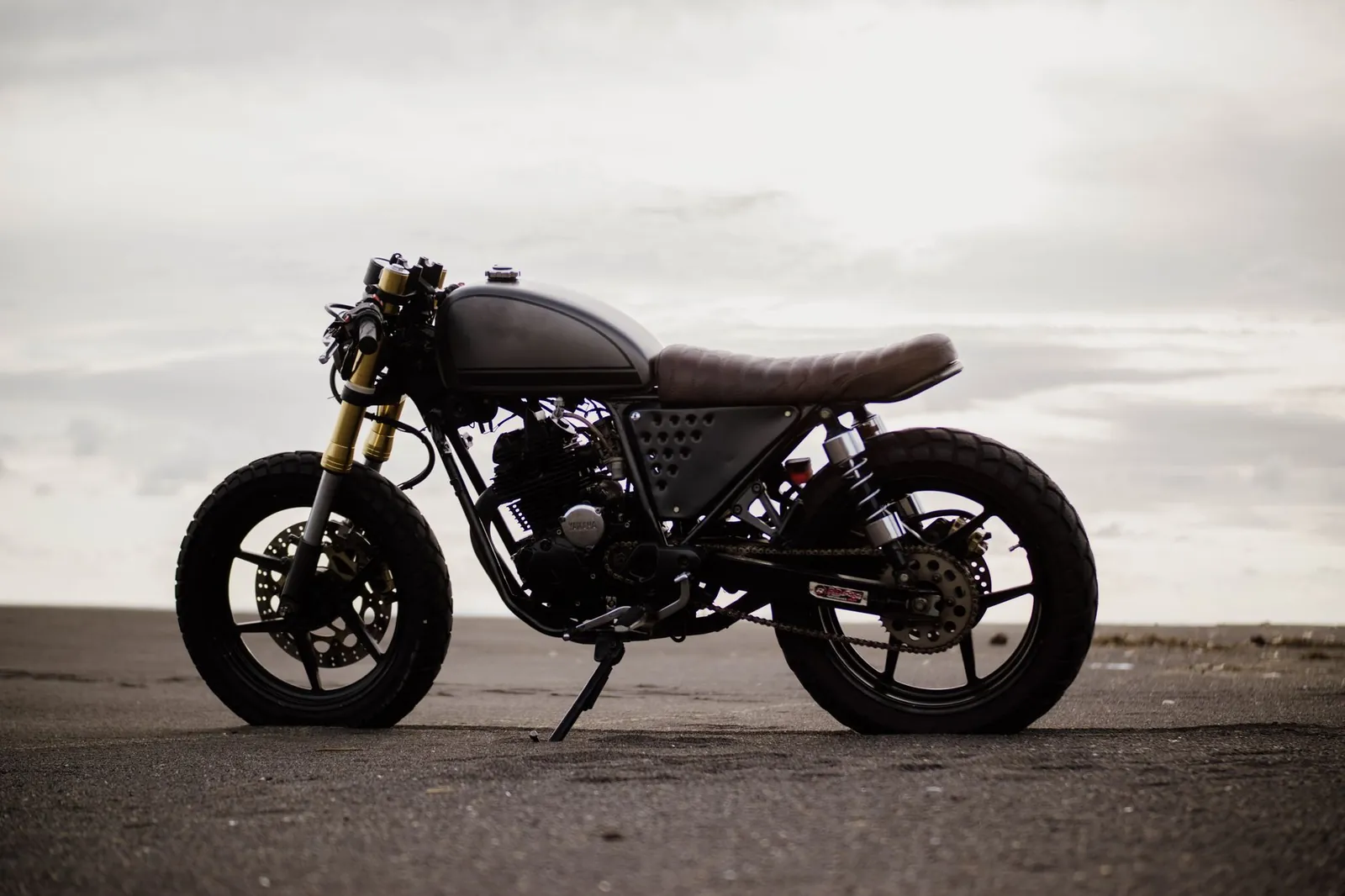 Side view of a vintage cafe racer motorcycle parked on an empty road under a cloudy sky. Stock photo illustrating Eicher Motors' product launched story.
