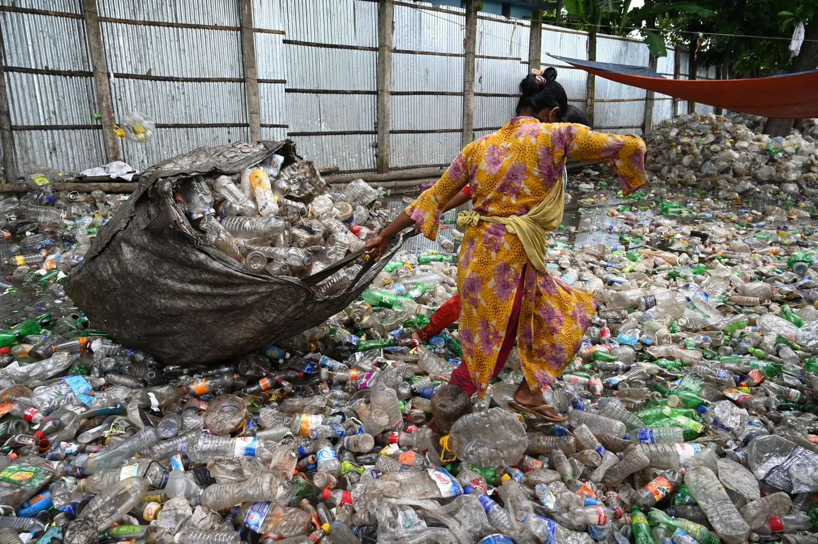 A worker in Chattogram sorts plastic bottles amidst a sea of waste, showcasing recycling efforts. Stock photo illustrating EKI Energy Services' expansion story.