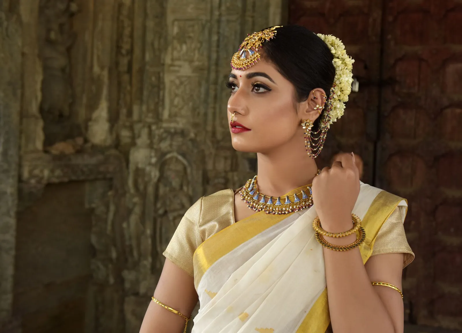 Beautiful Indian woman in traditional saree, adorned with exquisite jewelry, set against historic architecture. Stock photo illustrating P N Gadgil Jewellers' earning call story.