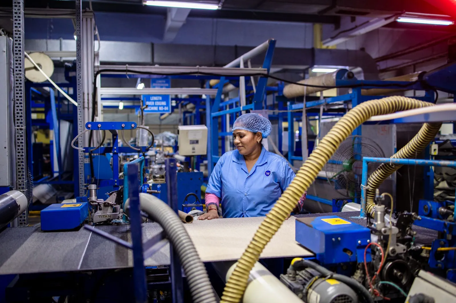 A female worker in a blue uniform operates machinery in a textile factory. Stock photo illustrating Shyam Metalics and Energy's financial results story.