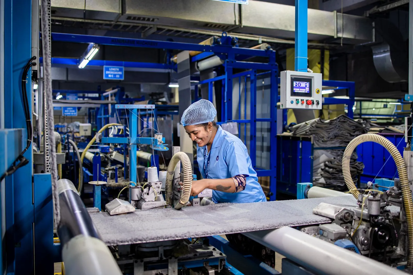 Indian female factory worker smiling while operating complex textile machinery in an industrial setting. Stock photo illustrating Greenply Industries' financial results story.