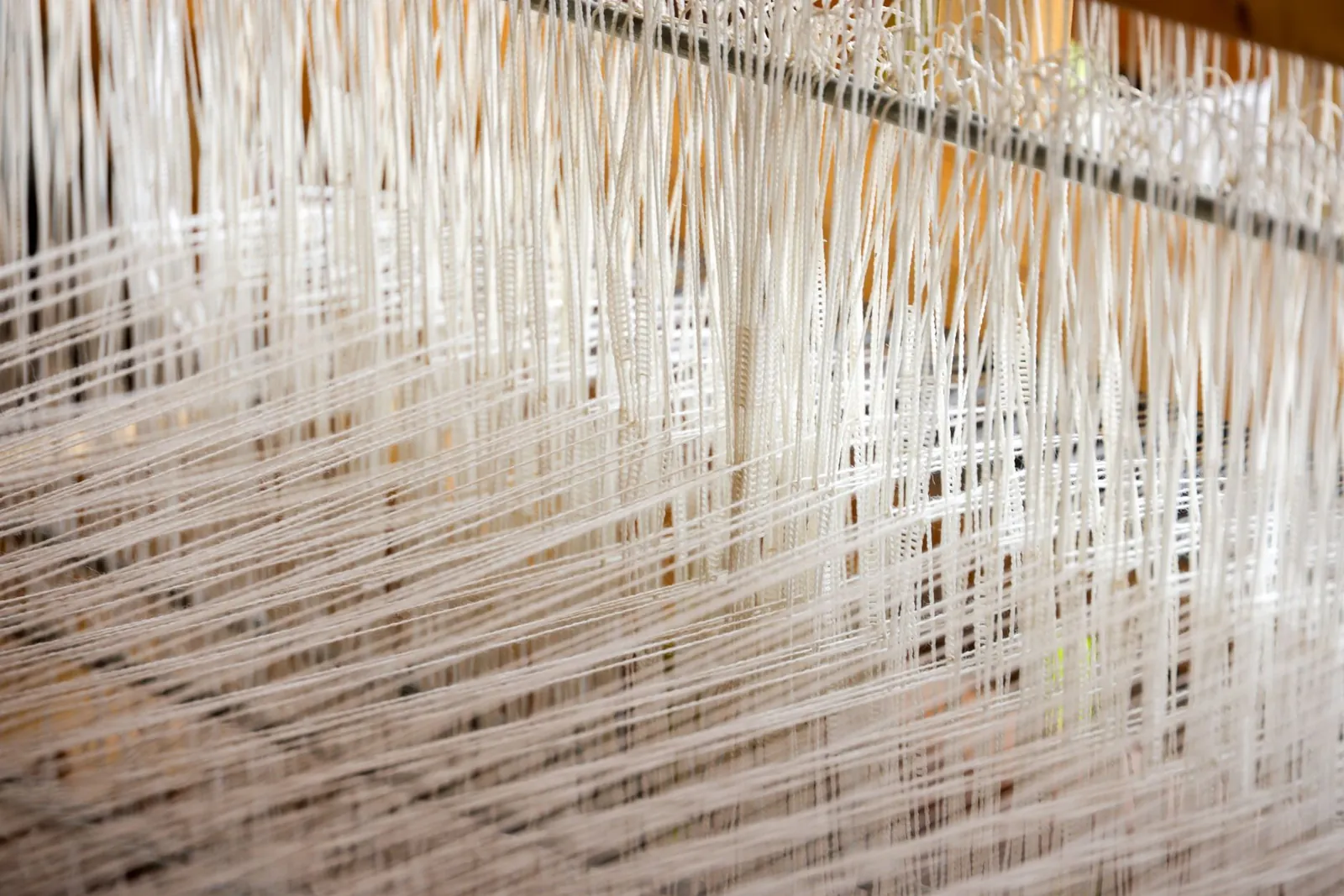 Detailed view of white threads woven on a loom, showcasing intricate textile work. Stock photo illustrating Aviva Industries' fund raise story.