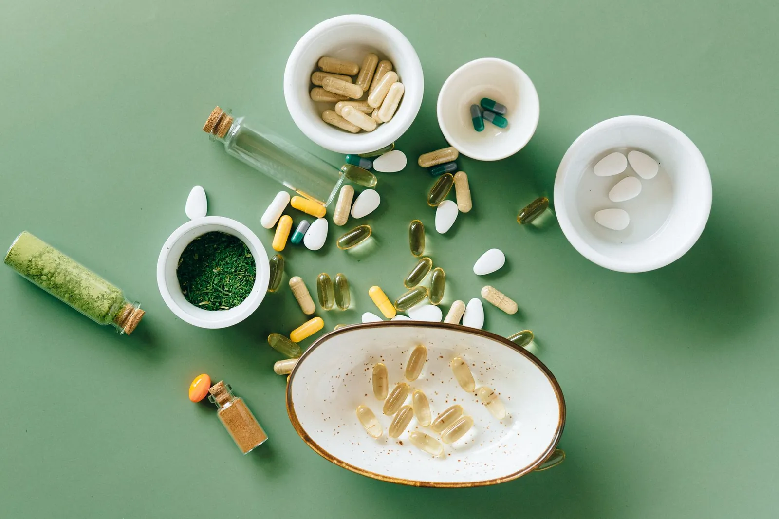 Top view of various herbal and pharmaceutical supplements in ceramic bowls on a green background. Stock photo illustrating Aayush Wellness' product launched story.