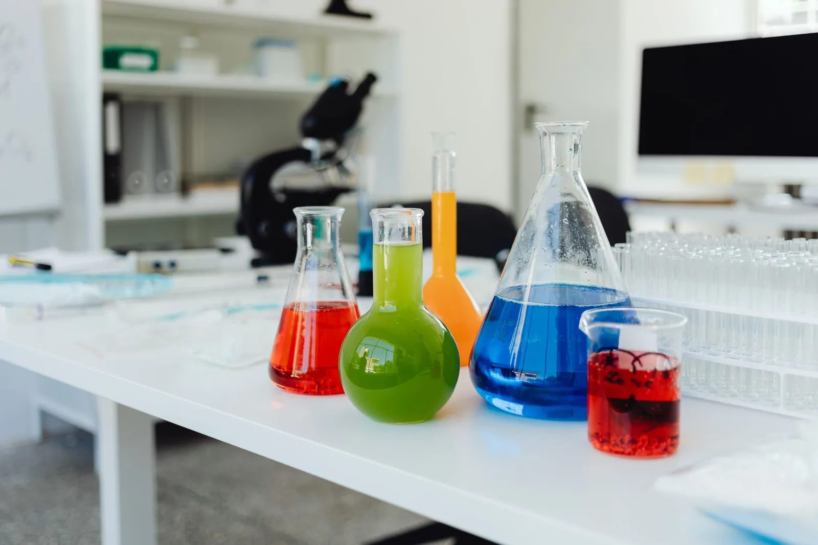 Bright, colorful chemicals in flasks and beakers on a lab table indicating a chemistry experiment in progress. Stock photo illustrating Chembond Material Technologies' financial results story.