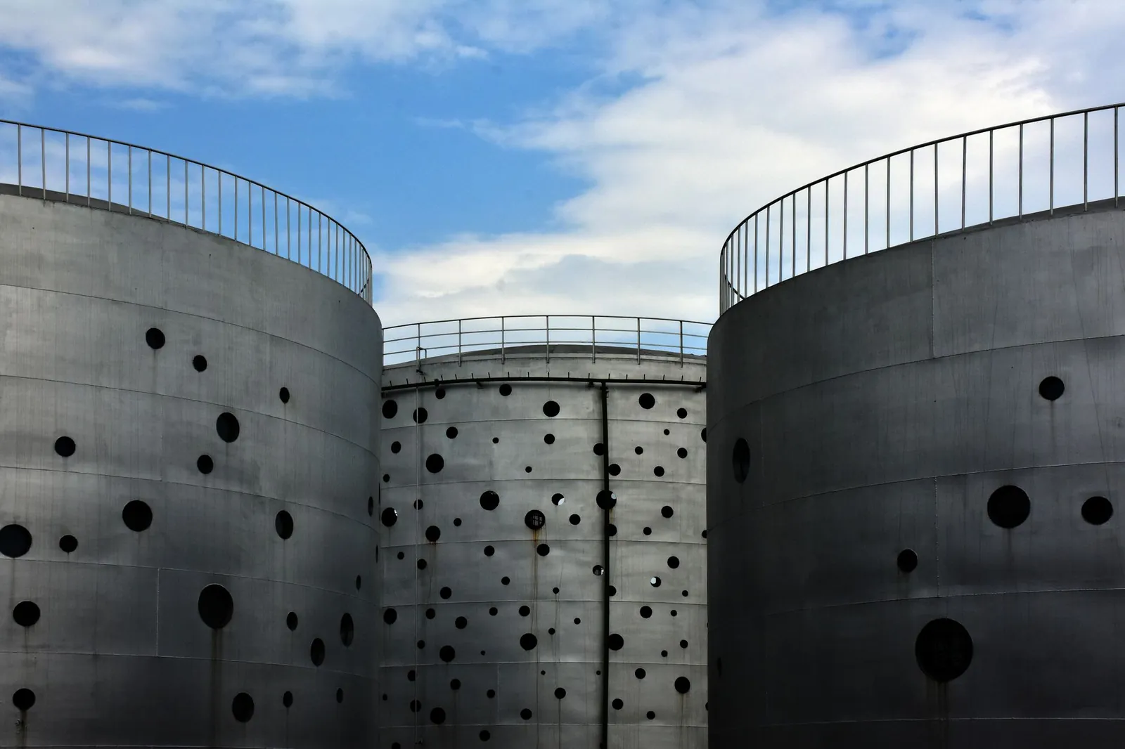 Large metal silos with perforated design standing under a clear blue sky in an industrial setting. Stock photo illustrating Nilachal Carbo Metalicks' new order story.