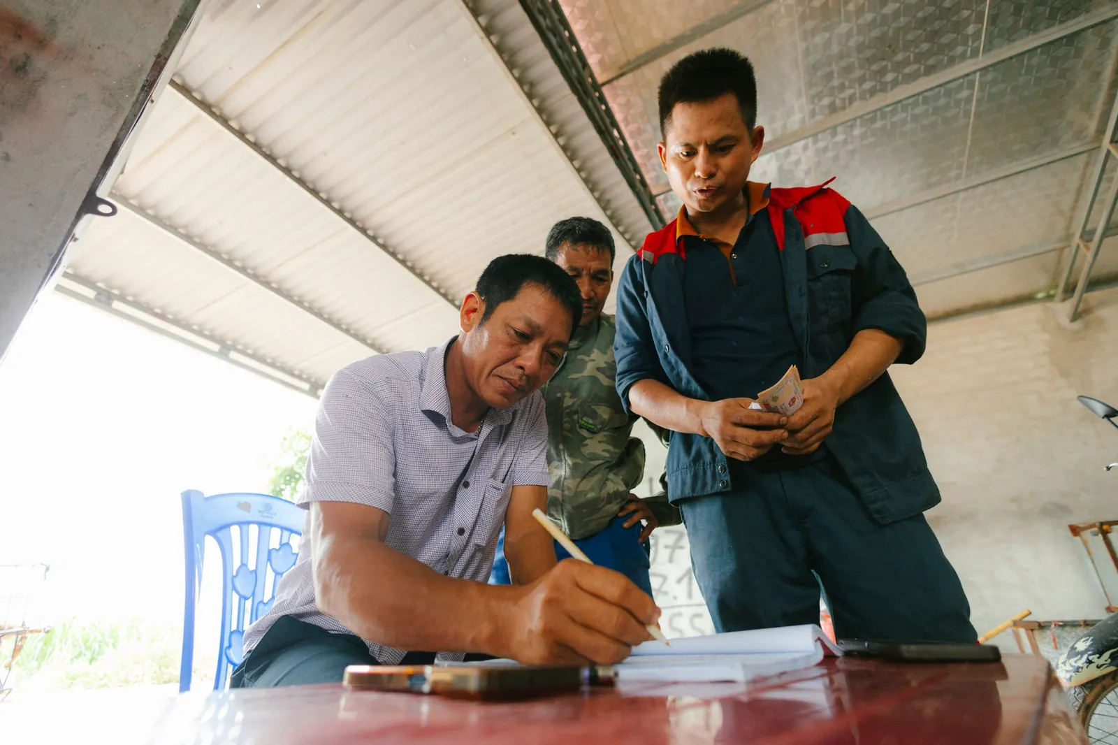 Three men involved in a financial transaction, with one signing documents indoors. Stock photo illustrating SMC Global Securities' fund raise story.
