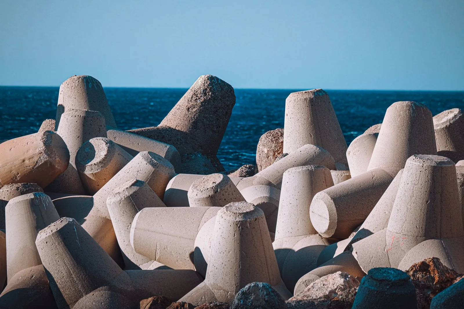 Concrete tetrapods form a solid breakwater against the blue sea under a clear sky. Stock photo illustrating Afcons Infrastructure's new order story.