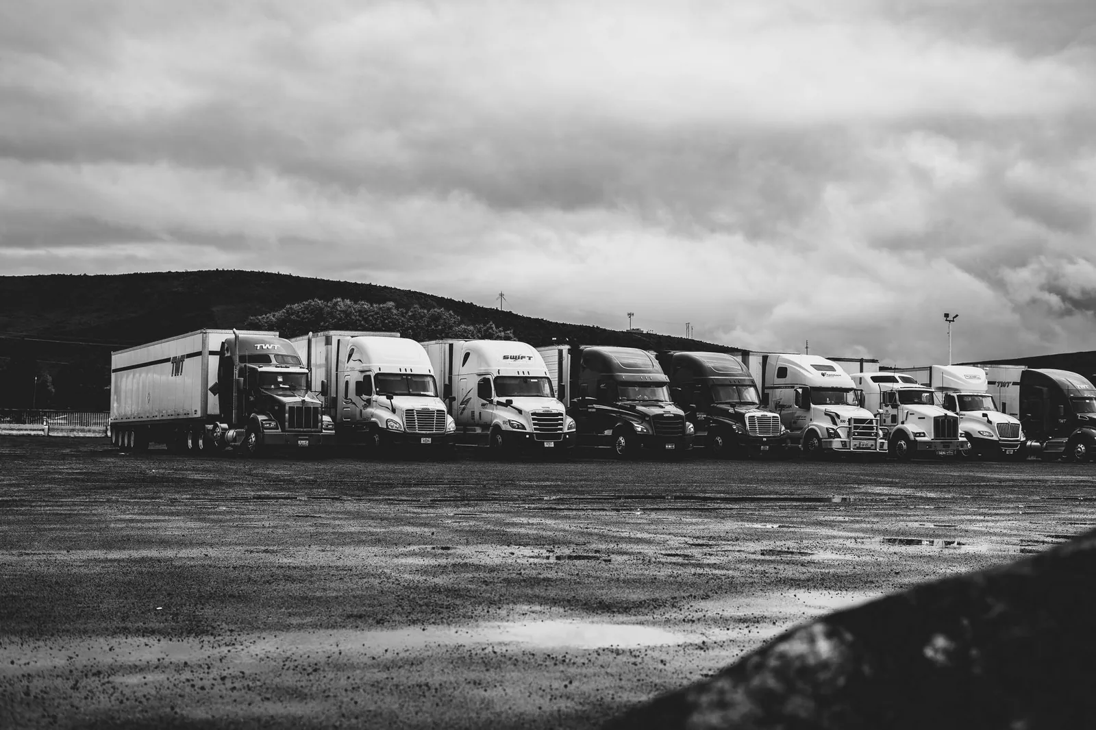 Row of parked semi trucks in a rainy lot, captured in a dramatic black and white setting. Stock photo illustrating Tata Motors' earning call story.
