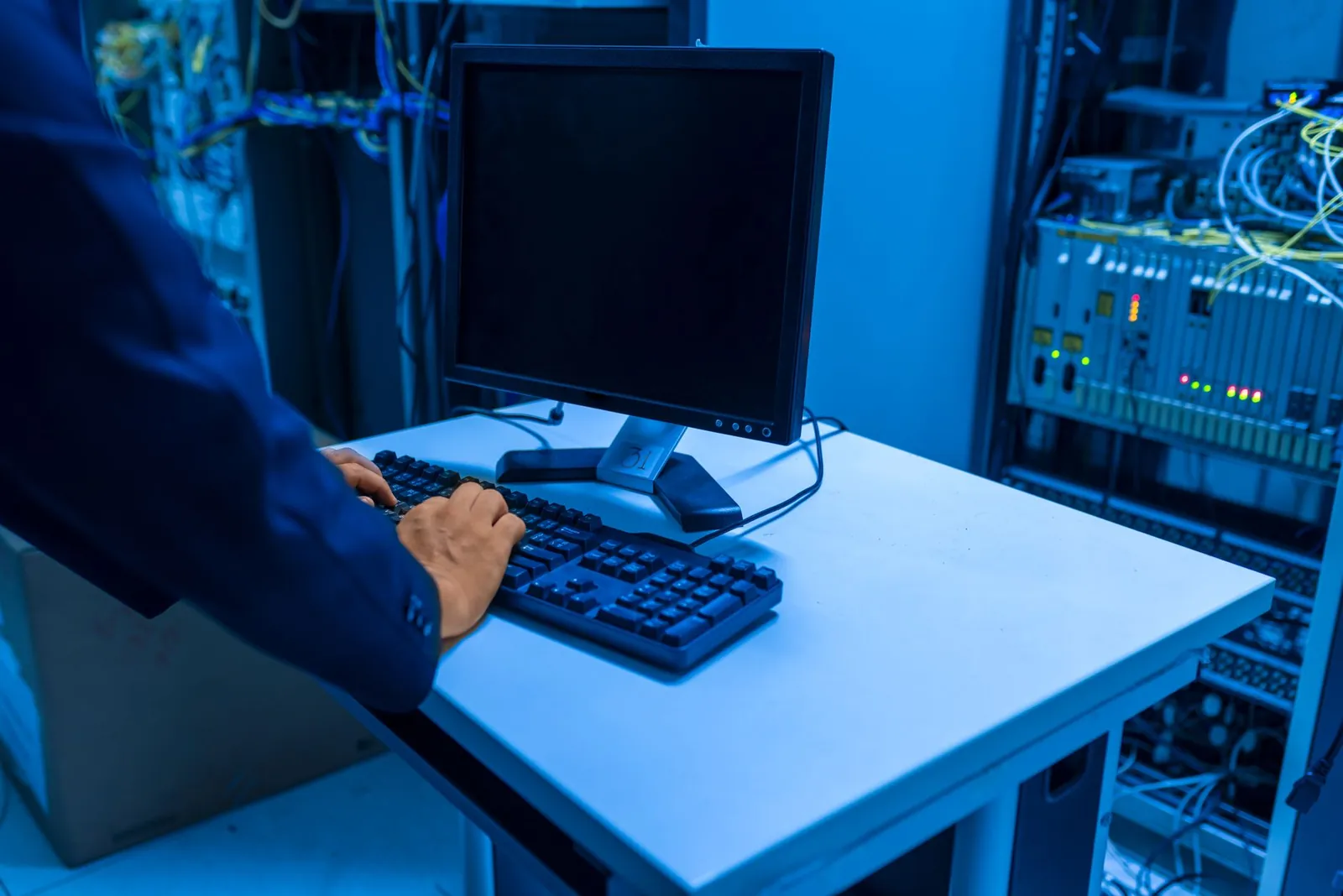An IT professional operates a computer in a server room, managing network systems and connected devices. Stock photo illustrating Valiant Communications' new order story.