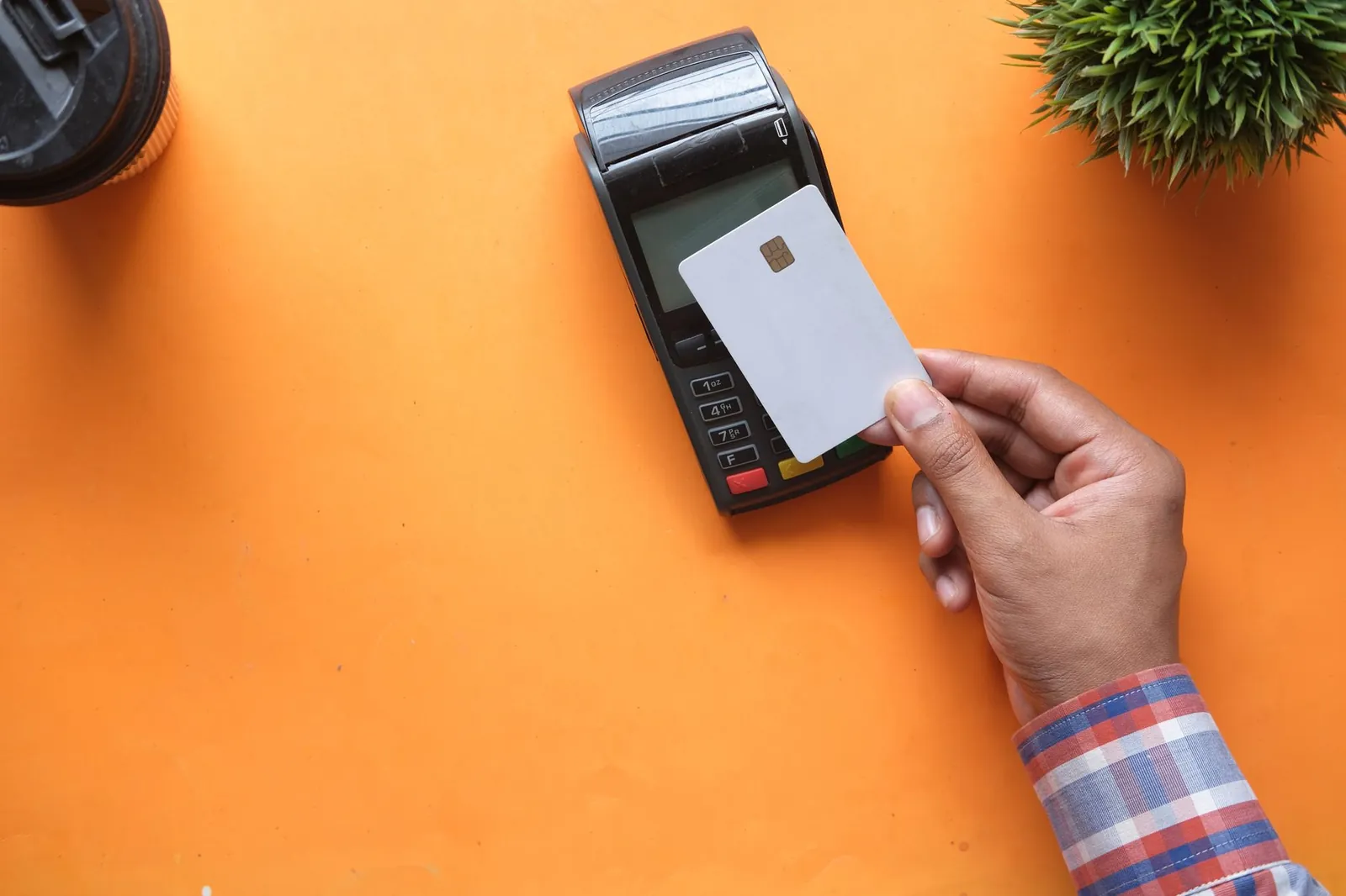 A person making a contactless payment with a credit card and card reader on a bright orange surface. Stock photo illustrating Pine Labs' partnership story.